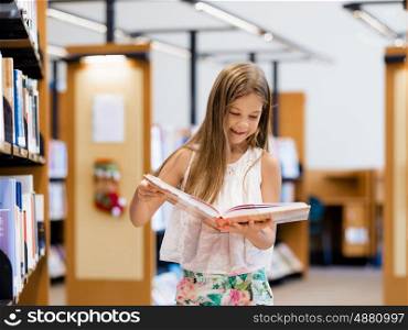 Little girl standing and reading books in library. I love reading