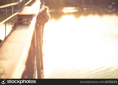 little girl standing on a on a bridge and looking down at the sunset beams