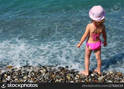 little girl stands on beach, rear view