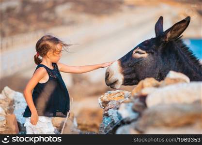 Little girl stroking a wild donkey outdoors. Little girl with donkey on the island of Mykonos