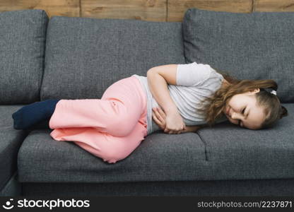 little girl suffering from stomach ache lying gray sofa
