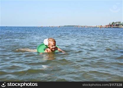 Little girl swimming on inflatable wheel against crowded beach