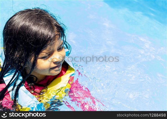 Little girl swimming with floaties, in the blue waters of a pool in the summer