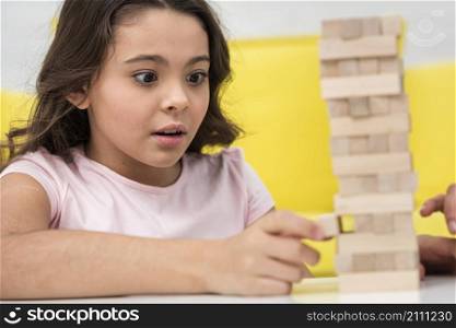 little girl taking care while getting piece wooden tower game