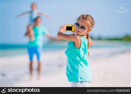 Little girl taking photo on phone of her family at the beach. Little girl making photo on phone of family at the beach