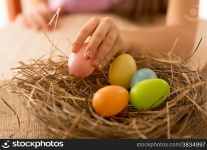 Little girl taking pink Easter egg from the nest