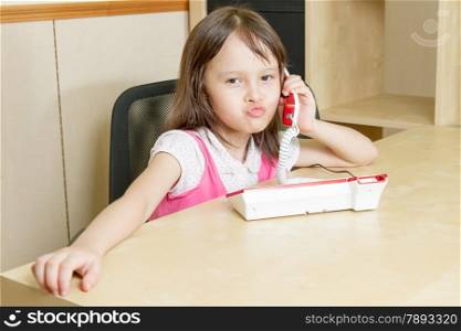 Little girl talking on red telephone at desk