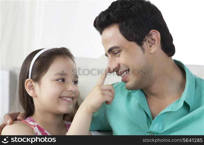 Little girl touching father&rsquo;s nose at home