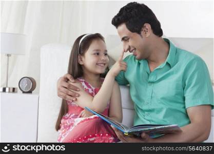 Little girl touching father&rsquo;s nose while sitting on sofa at home