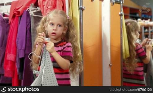 Little girl tries on clothes in fitting room of clothing store