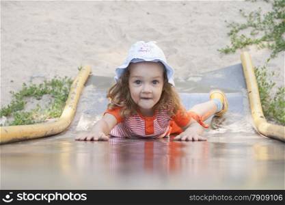 Little girl tries to climb the slope of the hill. Slide old metal, Soviet. Smiling girl.