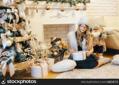 Little girl under Christmas tree with gift boxes at decorated living room with traditional fire place