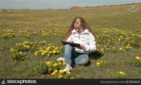 Little girl using a touch screen tablet PC on a meadow of wild peonies