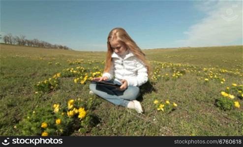 Little girl using a touch screen tablet PC on a meadow of wild peonies