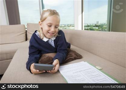 Little girl using calculator while studying on sofa
