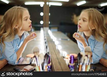 Little girl using lipstick at the mirror in makeup salon. Mom and daughter play stylists together, happy childhood, glamour family, make-up artist. Little girl using lipstick in makeup salon