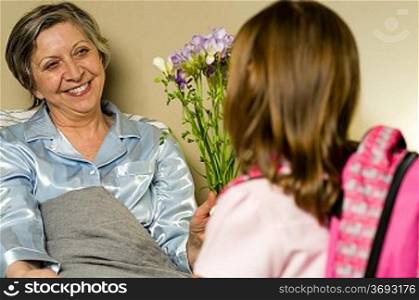 Little girl visiting her ill grandmother giving flowers