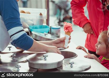 Little girl waiting for icecream. Mom buying a icecream her little daughter in a candy shop by the street. Young woman putting a scoop of pink icecream to a cone