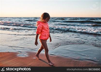 Little girl walking barefoot on a beach at sunset during summer vacation. Little girl walking barefoot on a beach at sunset
