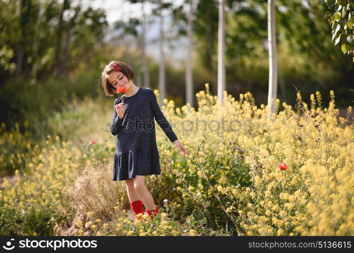 Little girl walking in nature field wearing beautiful dress with flowers in her hand.