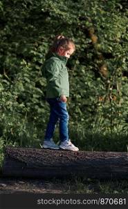 Little girl walking on stump in forest, playing during walk