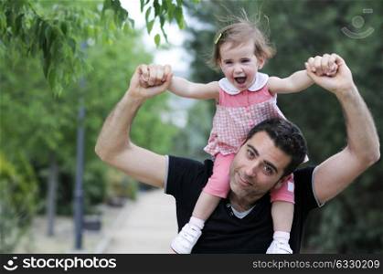 Little girl walking on the shoulders of her father in the park