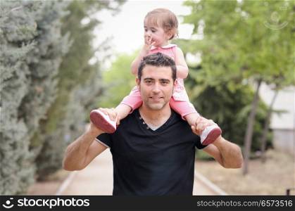 Little girl walking on the shoulders of her father in the park