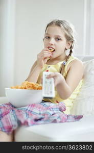 Little girl watching TV as she eats wheel shape snack pellets