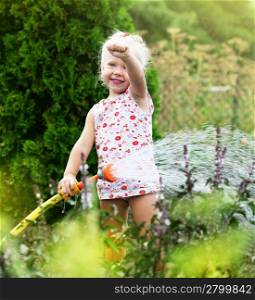 Little girl watering the grass in the garden