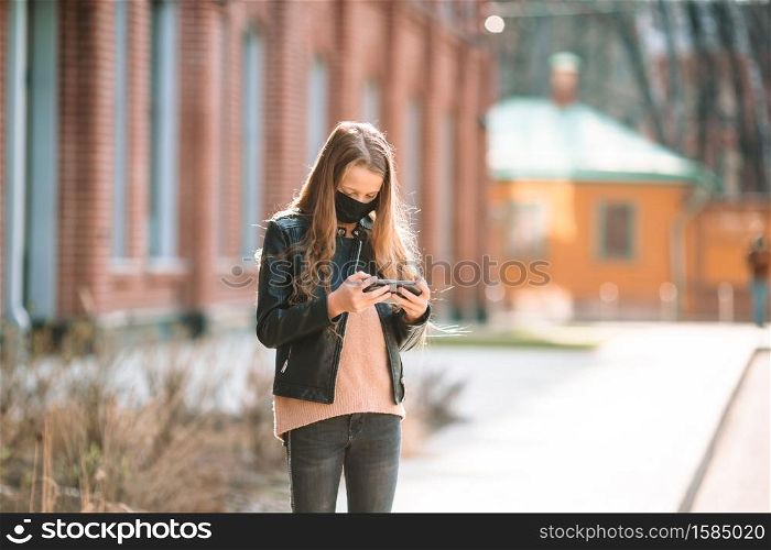 Little girl wearing a mask on the street in an empty city. Protection against Coronavirus and gripp. Girl wearing a mask on a background of a modern building,