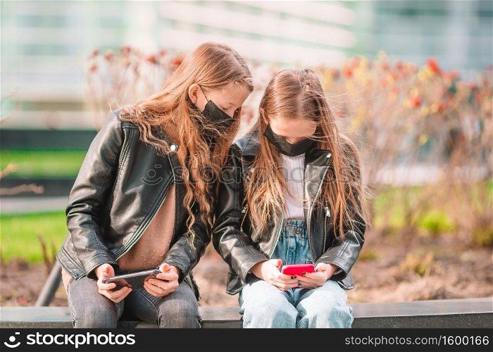 Little girl wearing a mask outdoors for prevent virus and playing smartphone. Protection against Coronavirus and gripp. Girl wearing a mask protect against Coronavirus and gripp