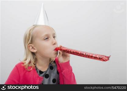 Little girl wearing party hat blowing noisemaker at home