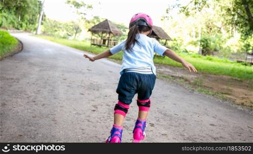 Little girl wearing protection pads and safety helmet learning to roller skate in summer park. Active outdoor sport for kids.