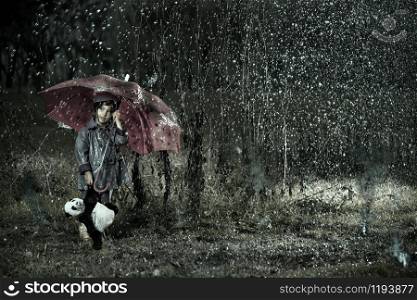 little girl wearing rain coat under a red umbrella with a panda bear toys under a stormy acid rain