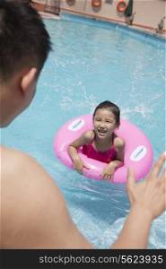Little girl with a pink tube and her father swimming in the pool