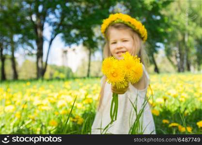 Little girl with a wreath of flowers. Little girl with a wreath od flowers on head, giving you bouquet of dandelions