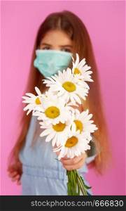 Little girl with allergies to flowers in a medical mask and a bouquet of daisies on a gently pink background. allergy flower mask
