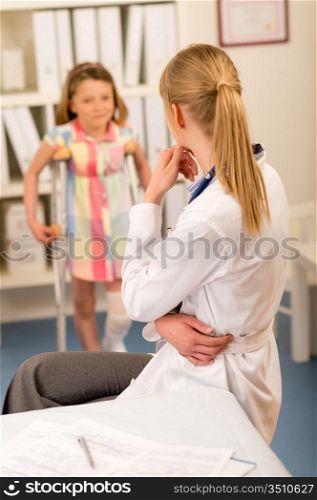 Little girl with bandaged leg standing with crutches surgery office