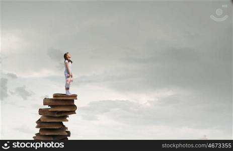 Little girl with bear. Cute girl wearing pajamas with toy bear in hand standing on pile of books