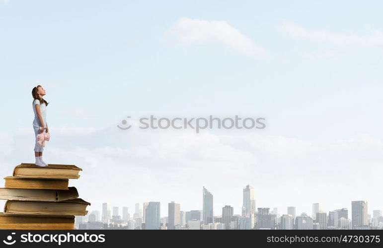 Little girl with bear. Cute girl wearing pajamas with toy bear in hand standing on pile of books