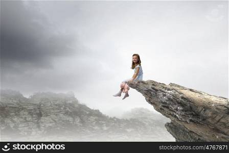 Little girl with bear. Cute girl wearing pajamas with toy bear in hand sitting on rock edge