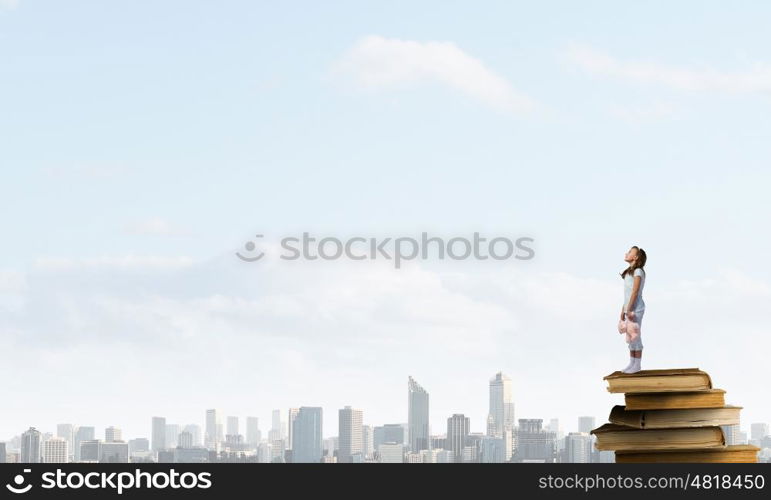 Little girl with bear. Cute girl wearing pajamas with toy bear in hand standing on pile of books