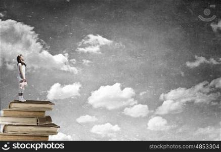 Little girl with bear. Cute girl wearing pajamas with toy bear in hand standing on pile of books