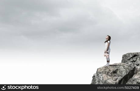 Little girl with bear. Cute girl wearing pajamas with toy bear in hand standing on rock edge