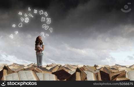 Little girl with bear. Cute girl wearing pajamas with toy bear in hand standing on pile of books