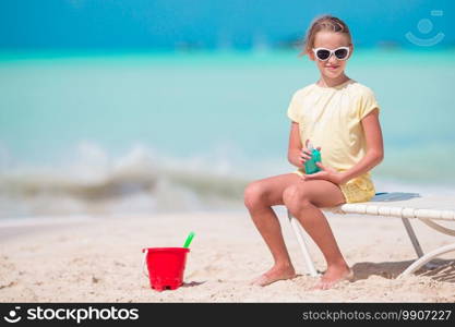 Little girl with bottle of sun cream sitting at tropical beach. Beautiful kid with bottle of sun cream on tropical beach