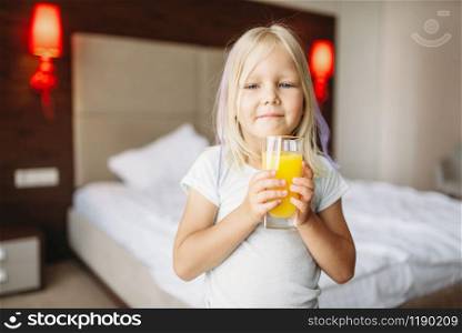 Little girl with glass of fresh orange juice in bedroom at home. A truly carefree childhood, happy time