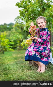 Little girl with grapes in the garden. Happy cute baby eating grapes.. Little girl with grapes in the garden.