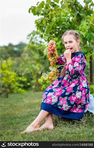 Little girl with grapes in the garden. Happy cute baby eating grapes.. Little girl with grapes in the garden.