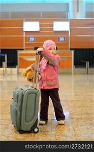 little girl with grey suitcase standing alone at airport